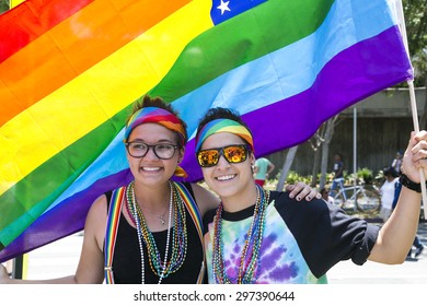 West Hollywood, Los Angeles, California, USA, June 14, 2015, 40th Annual Gay Pride Parade For LGBT Community, Down Santa Monica Blvd., Two Lesbian Women Under Gay Rainbow Flag Smile