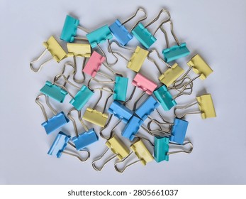 West Java, Indonesia - June 5, 2026 : A scattered pile of colorful binder clips on a white background with ample copy space, various shades of pastel blue, teal, yellow, and soft pink metal office clips with silver wire handles, scattered in a loose, artistic cluster filling the frame. Set against a seamless, bright white surface, related to office organization, paper management, school supplies, project planning, brainstorming, and professional workspace themes. The clean, neutral background makes it easy to integrate into various designs, presentations, or advertising layouts