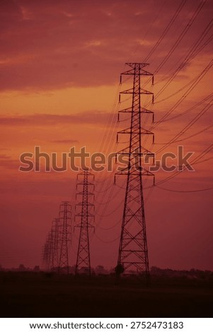 West Java, Indonesia - Perspective view of high voltage transmission towers row against a dramatic red sunset sky, Shot with a vertical (portrait) orientation and a focus on perspective, emphasizing the height and the receding line of the towers.