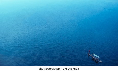 West Java, Indonesia - Top-down perspective of a lone fisherman on a bamboo raft on vast blue water, symbolizing simplicity, hard work, and the solitary journey toward opportunity.