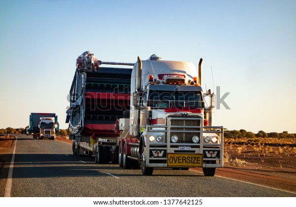 WESTERN AUSTRALIA - JULY 11, 2018: White\
Western Star truck with red stripes driving on an outback road in\
Western Australia with an oversize\
cago