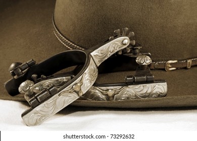 Western or cowboy themed image of a cowboy hat and fancy spurs on a white surface (sepia tint added)