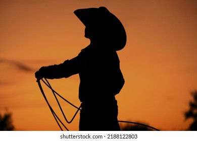 Western Culture Shows Silhouette Of Child Cowboy Practicing In Sunset With Rope For Rodeo Roping Lifestyle On Ranch.
