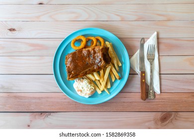 Western Food On Table - BBQ Pork Ribs, Onion Rings, French Fries And Coleslaw In Blue Plate