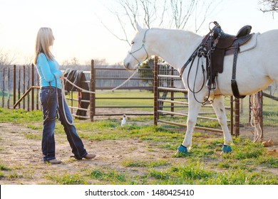 Western industry lifestyle shows woman with gray mare horse on halter with saddle for ride.