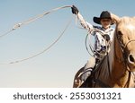 Western industry with young cowboy horseback on palomino closeup swinging rope in air, copy space on background for ranch rodeo concept.