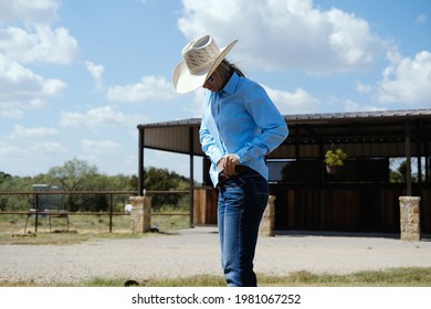 Western lifestyle on ranch in agriculture industry shows lifestyle portrait on cowgirl tucking in shirt for labor work.