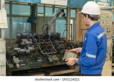 Western man, caucasian, an engineer or worker control the smart robot welding hand system automated manufacturing machine engine in factory, industry equipment in operation warehouse. People.