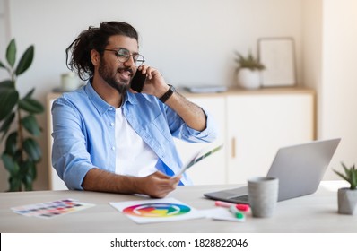 Western Man Freelance Designer Talking On Cellphone With Client, Discussing Future Project, Sitting At Desk In White Home Office With Color Swatches, Choosing Gamma For Interior, Copy Space