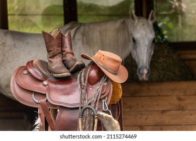 Western Riding Scenery: A Western Saddle, Western Boots And A Cowboy Hat With A Horse In The Background