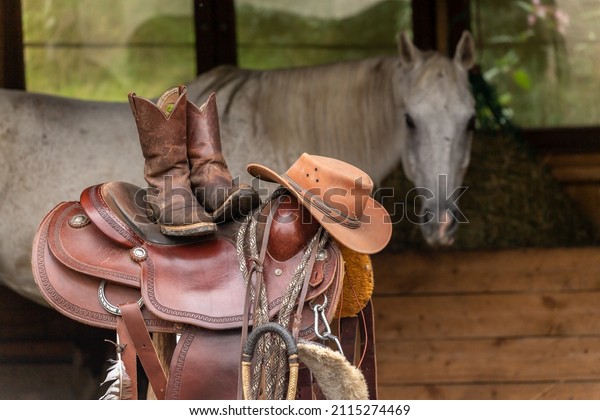 Western riding scenery: A\
western saddle, western boots and a cowboy hat with a horse in the\
background