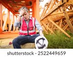 Western white ethnicity worker is resting and drinking water from bottle after working for many hours in a very hot day. Thirsty - tired caucasian foreman or construction worker sitting on the floor.