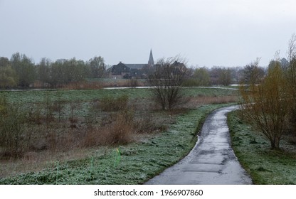 Wet Asphalt Road In A Wetland Nature Reserve With Bare Trees, Grass And A Snow Storm