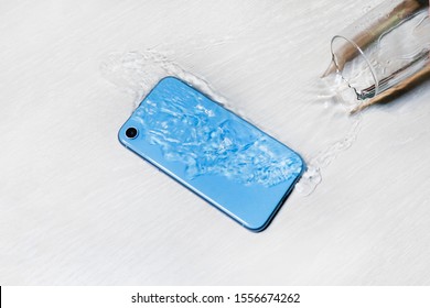 Wet blue smartphone in water on table, floor. Accident with cell mobile phone, water flowing from spilled glass.