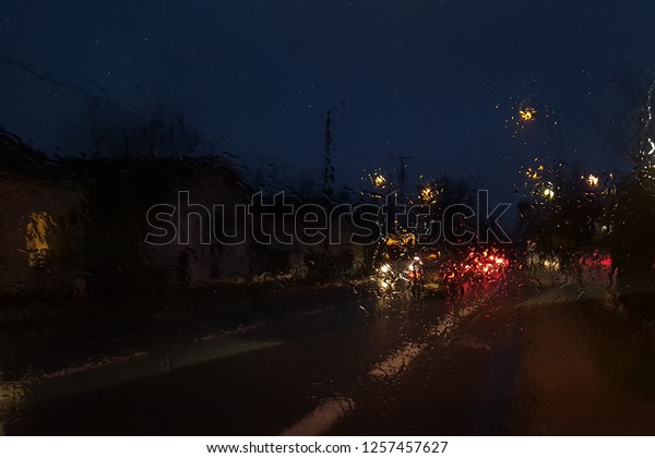 Wet car window with the\
background of the night city traffic rain fall at night with blurry\
cars 