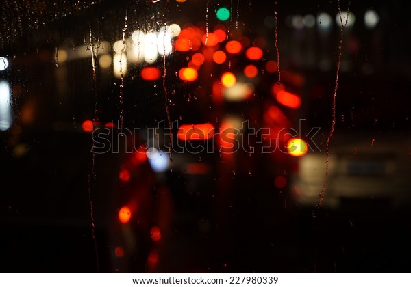 Wet the car window with the\
background of the night city traffic and traffic congestion\
concept.