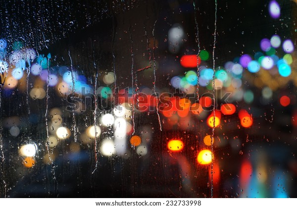 Wet the car window with the\
background of the night city traffic and traffic congestion\
concept.
