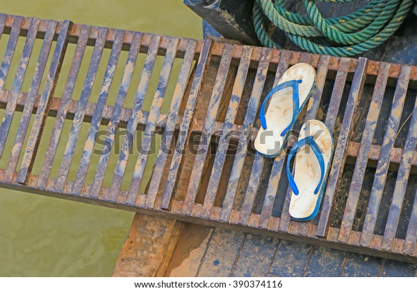 Wet\
dirt on white and blue rubber slippers on a portable metal gangway\
bridge connecting to the boat on Mekong River,\
Laos\
