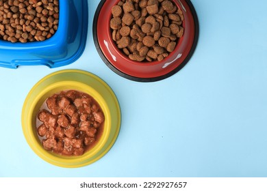 Wet and dry pet food in feeding bowls on light blue background, flat lay. Space for text