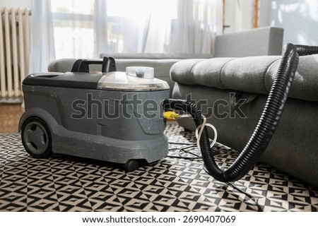 Wet extractor machine cleaning gray sofa and geometric patterned carpet in a living room