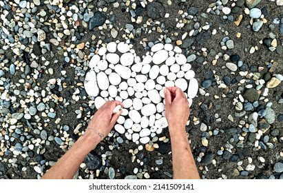 Wet Female Hands Holding White Stones, Creating Heart Shape On Wet Pebbles In The Beach.