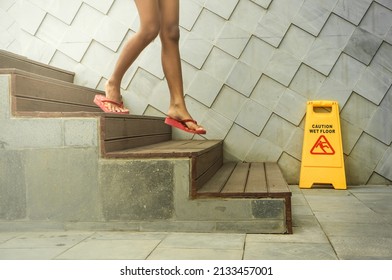 Wet floor sign board placed beside wooden stairs at swimming pool with a teen girl stepping down the stairs - Powered by Shutterstock