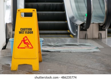 A Wet Floor Sign And Bucket At A Spill In Front Of An Escalator.