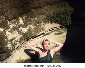 Wet Girl Emerging From The Water Against The Backdrop Of A Rock Illuminated By The Sun's Rays