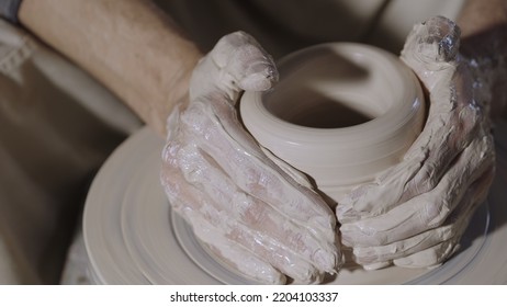 Wet male potter's hands sculpting soft clay and shaping the pot on potters wheel. Master gives shape to the pottery in a creative workshop. Creative masterclass from an artisan. Clay shaping close up. - Powered by Shutterstock