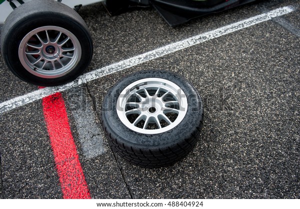 Wet motor sport racing tire on\
asphalt near single seater car with different tire\
mounted