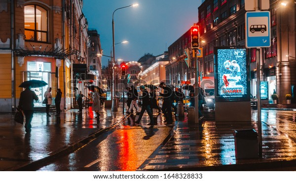 Wet night city street rain bokeh reflection bright
colorful lights puddles pavement lights car lighting. Pedestrians
on a pedestrian crossing under an umbrella. Russia Moscow 05
November 2019.
