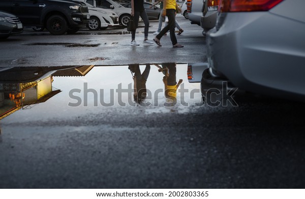 Wet parking spaces after hard rain fall with\
reflection of cars and walking people in puddle on the ground\
.Selective focus.