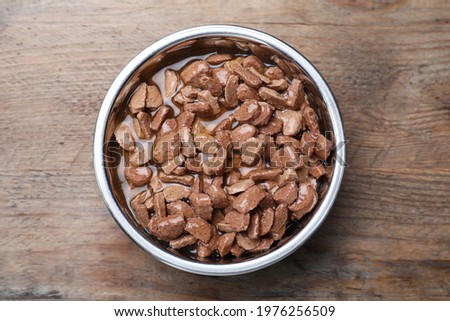Wet pet food in feeding bowl on wooden table, top view