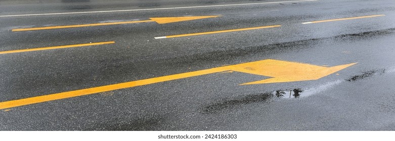 A wet road with yellow arrows on the asphalt.