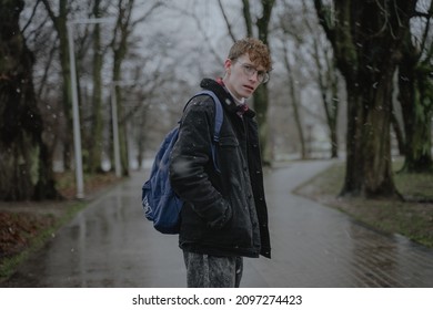 Wet Snow, Rainy Winter Outside, Cloudy Weather, A Stylish Young Man With Curly Hair And Round Glasses For Vision Is Standing In The Middle Of The Park, Looking At The Camera