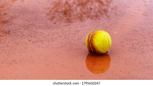 Wet Tennis Ball In Puddle On Outdoor Clay Tennis Court In Rainy Weather. Cancellation Of Match Or End Of Season For Outdoor Sports. Panoramic Size. Banner. Copy Space