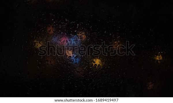 Wet the window with the\
background of the night city colorful lights. Concept. Close up of\
window covered by rain drops with street blurred lights behind\
it.