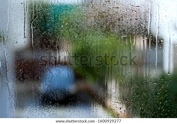 Wet window glass with rain drops, water drippings\
and a blurred street view