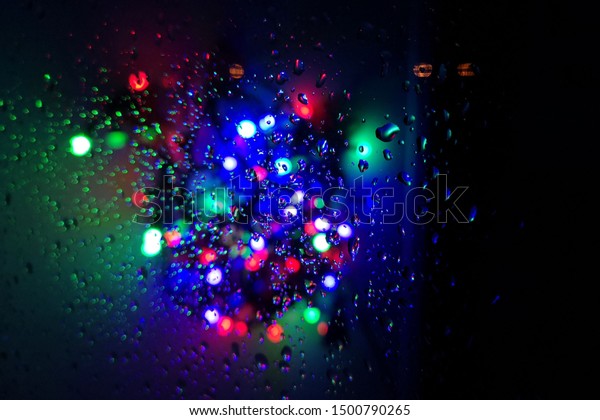 Wet window with night city background.\
Multicolored blurred lights. Autumn\
background