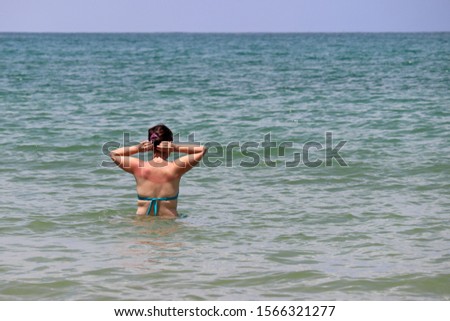 Wet woman with sunburned shoulders fixes her hair during swimming in a tropical ocean. Concept of sea vacations, holidays and enjoying the water