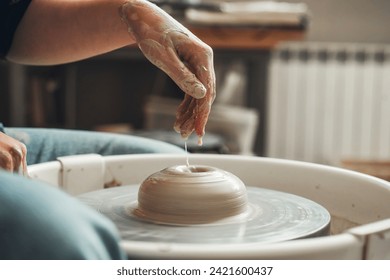 Wetting a clay product with water on a potter's wheel. Pottery, female hands of a potter creating a product from white clay. - Powered by Shutterstock