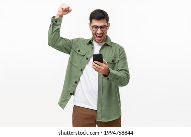 We've Got A Winner! Happy Young Man In Green Shirt Looking At Phone Screen With Victory Expression, Isolated On Gray Background