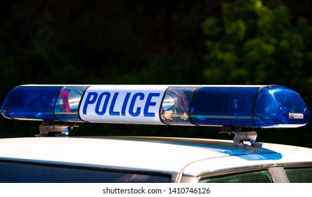 Weybridge, UK. 12th May 2019. View Of Police Sign With Blue Lights Atop A Patrol Car Against A Background Of Green Bushes.