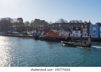 A Weymouth Lifeboat Being Hosed Down In The Harbour With Coastal Explorer Tour Rib Boat Going Past On A Sunny Morning With Blue Sky. Weymouth, Dorset, England. Taken On 16th April 2021