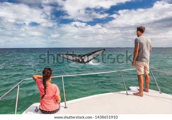 Whale watching boat tour\
tourists people on ship looking at humpback tail breaching ocean in\
tropical destination, summer travel vacation. Couple on deck of\
catamaran.