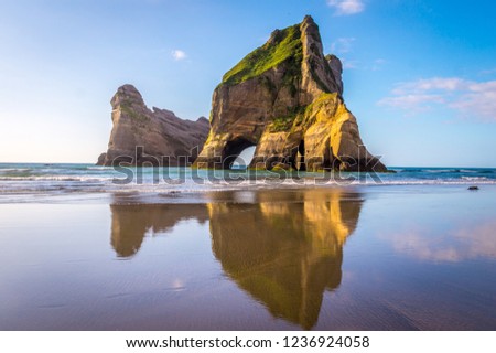 Wharariki Beach, New Zealand: Beautiful rock formations reflect in the water as mighty waves clash against the shore. This vast stretch of coast displays natural beauty in so many ways.