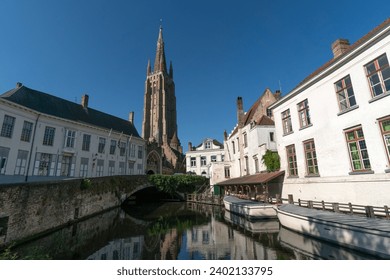 Wharf on the canal since Dijver park with the Our Lady church tower reflected on the canal in the old town of the beautiful city of Brugge in Belgium in a sunny day.
