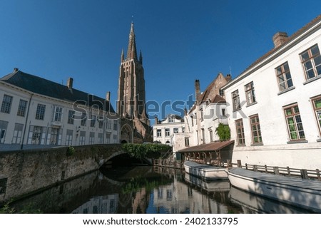 Wharf on the canal since Dijver park with the Our Lady church tower reflected on the canal in the old town of the beautiful city of Brugge in Belgium in a sunny day.