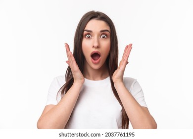 What an amazing news. Surprised and astonished, excited young woman react to something awesome happened, gasping, open mouth and raise hands near face, staring camera, white background