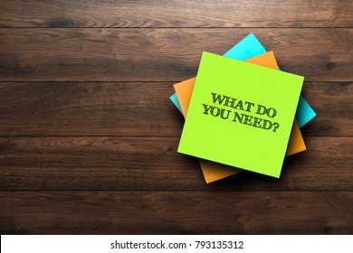 What Do You Need, the phrase is written on multi-colored stickers, on a brown wooden background. Business concept, strategy, plan, planning.